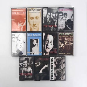 May include: A collection of eleven The Smiths music cassette tapes arranged in a grid. The covers feature various black and white or tinted photographic portraits and graphic designs, each clearly displaying the band name The Smiths in red or white text.