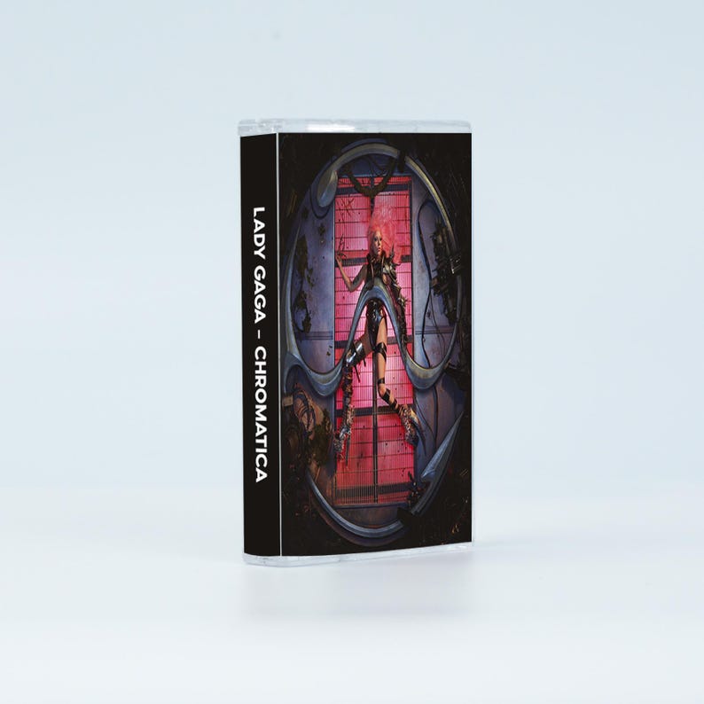 May include: A cassette tape case featuring the album cover for Lady Gaga - Chromatica. The cover art displays a figure in a dark, metallic, circular structure against a bright pink grid background. The spine text reads LADY GAGA - CHROMATICA.