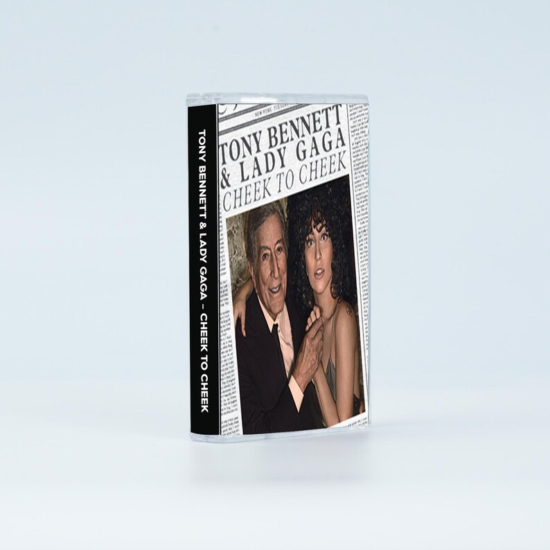 May include: A cassette tape case featuring the album cover for Tony Bennett & Lady Gaga's Cheek to Cheek. The cover design mimics a newspaper layout with the artists' names and album title in bold black text above a photograph of the two musicians.
