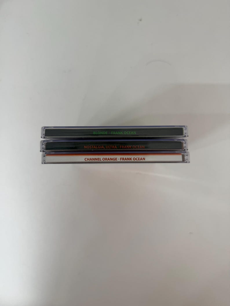 May include: Three compact disc cases stacked on top of each other. The top case is labeled "BLONDE - FRANK OCEAN" in white text on a black background. The middle case reads "NOSTALGIA, ULTRA - FRANK OCEAN". The bottom case is labeled "CHANNEL ORANGE - FRANK OCEAN".