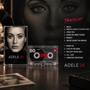 May include: A clear plastic cassette tape with a black label featuring the number 50 and the word ZAPAS in red. Next to it is a cassette case with a portrait of Adele and the text ADELE 25. A tracklist is printed on the right with 11 song titles.