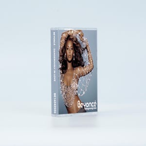 May include: A cassette tape case featuring the album Dangerously in Love by Beyonc&eacute;. The cover art displays a photograph of the artist wearing a silver beaded top. The text Beyonc&eacute; and Dangerously in Love is printed on the front and side.
