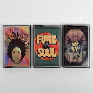 Może przedstawiać: Trzy stare kasety magnetofonowe z kolorowymi wzorami. Jedna przedstawia twarz kobiety z instrumentami muzycznymi, druga mówi "Funk & Soul", a ostatnia "Funk Music" z palmami. Kasety są w przezroczystych plastikowych etui.