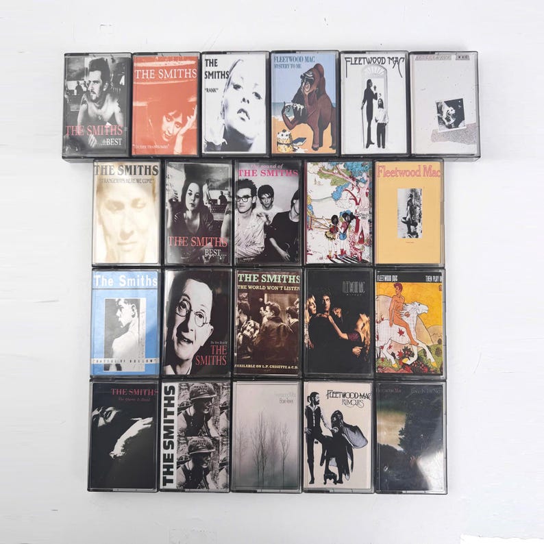 May include: A collection of twenty-eight music cassette tapes arranged in a grid, featuring various album covers by The Smiths and Fleetwood Mac. The plastic cases display diverse graphic designs, band photography, and text titles including The Smiths and Fleetwood Mac.