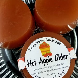 May include: Three round bars of brown soap with a white label that reads "Humphrey's Handmade Hot Apple Cider Glycerine soap, argan oil, calendula extract sunflower extract, aloe leaf extract, fragrance Handcrafted Soap".