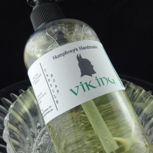 May include: A clear bottle of green liquid with a white label that says "Humphrey's Handmade Castile Soap Viking". The label also features a black silhouette of a Viking helmet.