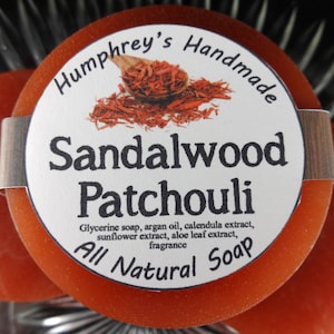 May include: A round, orange soap bar with a white label that reads "Humphrey's Handmade Sandalwood Patchouli Glycerine soap, argan oil, calendula extract, sunflower extract, aloe leaf extract, fragrance All Natural Soap".