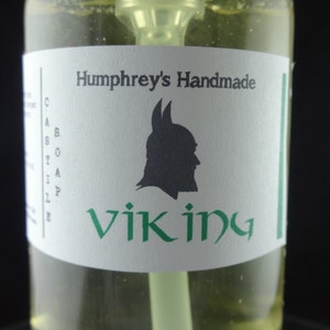 May include: A clear glass bottle with a white label that says "Humphrey's Handmade Viking" with a black silhouette of a Viking wearing a helmet. The label has a green border.