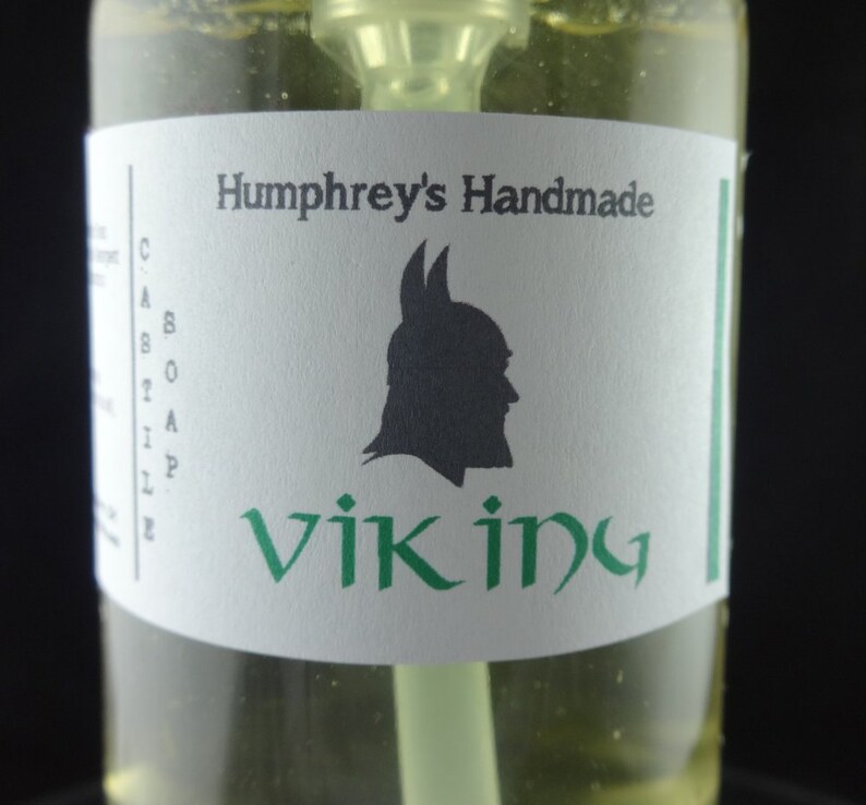 May include: A clear glass bottle with a white label that says "Humphrey's Handmade Viking" with a black silhouette of a Viking wearing a helmet. The label has a green border.