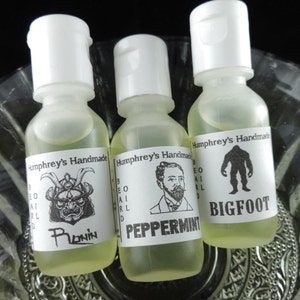 May include: Three small glass bottles with white caps and labels. The labels are white with black text and images. The bottles contain beard oil. The labels read "Humphrey's Handmade Beard Oil" and the scents are "Ronin", "Peppermint", and "Bigfoot".