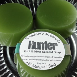 May include: Two green handmade soap bars with a white label that reads "Humphrey's Handmade Hunter Dirt & Moss Scented Soap Glycerine soap(with added argan oil, calendula extract sunflower extract, aloe leaf extract), fragrance All Natural Soap"