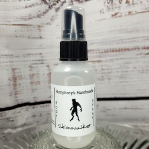 May include: A clear body spray bottle with a black pump and cap. The label reads "Humphrey's Handmade" with a silhouette of a creature and the word "Skinwalker". The bottle is sitting on a clear, decorative surface.