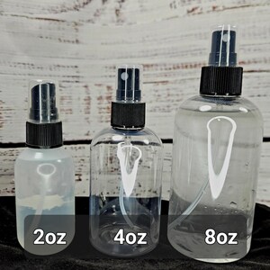 May include: Three clear spray bottles of varying sizes, labeled 2oz, 4oz, and 8oz. Each bottle has a black spray nozzle and a clear plastic cap. The bottles are filled with a clear liquid and are arranged against a light wood background.