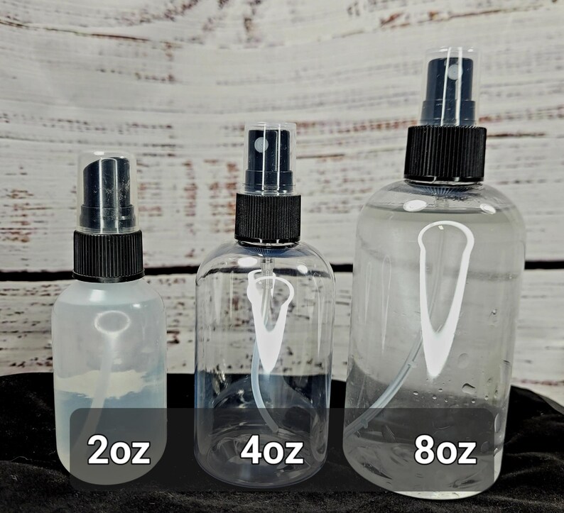 May include: Three clear spray bottles of varying sizes, labeled 2oz, 4oz, and 8oz. Each bottle has a black spray nozzle and a clear plastic cap. The bottles are filled with a clear liquid and are arranged against a light wood background.