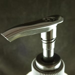 May include: A black pump bottle with a silver top and a curved spout. The pump is made of metal and has a shiny finish.