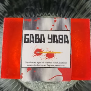 May include: A rectangular red glycerin soap bar with a white label featuring the Cyrillic text "БАВА УАЗА". The label includes a pencil and red splatter design. Ingredients listed include argan oil and aloe leaf extract.