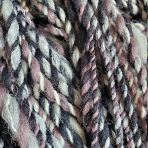 May include: A close-up of a skein of yarn with a mix of black, white, and purple shades. The yarn is soft and fluffy, and it is perfect for knitting or crocheting.
