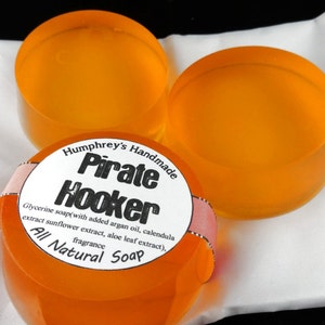 Pu&ograve; includere: Tre saponette di colore arancione fatte a mano con un'etichetta che recita "Humphrey's Handmade Pirate Hooker Glycerine soap(with added argan oil, calendula extract sunflower extract, aloe leaf extract), fragrance All Natural Soap"