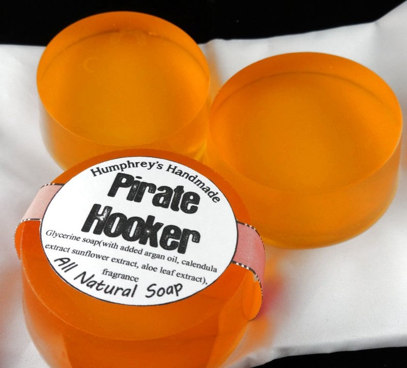 Pu&ograve; includere: Tre saponette di colore arancione fatte a mano con un'etichetta che recita "Humphrey's Handmade Pirate Hooker Glycerine soap(with added argan oil, calendula extract sunflower extract, aloe leaf extract), fragrance All Natural Soap"