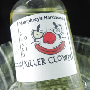 May include: A clear glass bottle with yellow liquid inside. The label reads "Humphrey's Handmade" and features a cartoon clown face with the words "BEARD" and "KILLER CLOWN". The bottle is partially submerged in a clear glass bowl.