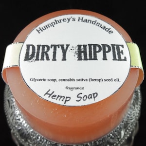 May include: A round bar of orange soap with a white label that reads "Humphrey's Handmade Dirty Hippie Glycerin soap, cannabis sativa (hemp) seed oil, fragrance Hemp Soap".