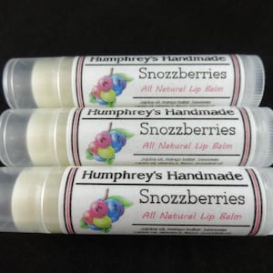 May include: Three clear tubes of lip balm with white labels. The labels have pink and black stripes and say "Humphrey's Handmade Snozzberries All Natural Lip Balm" with a picture of colorful berries. The ingredients are listed as "Jojoba oil, mango butter, beeswax, castor oil, vitamin E, flavor, essential oil."