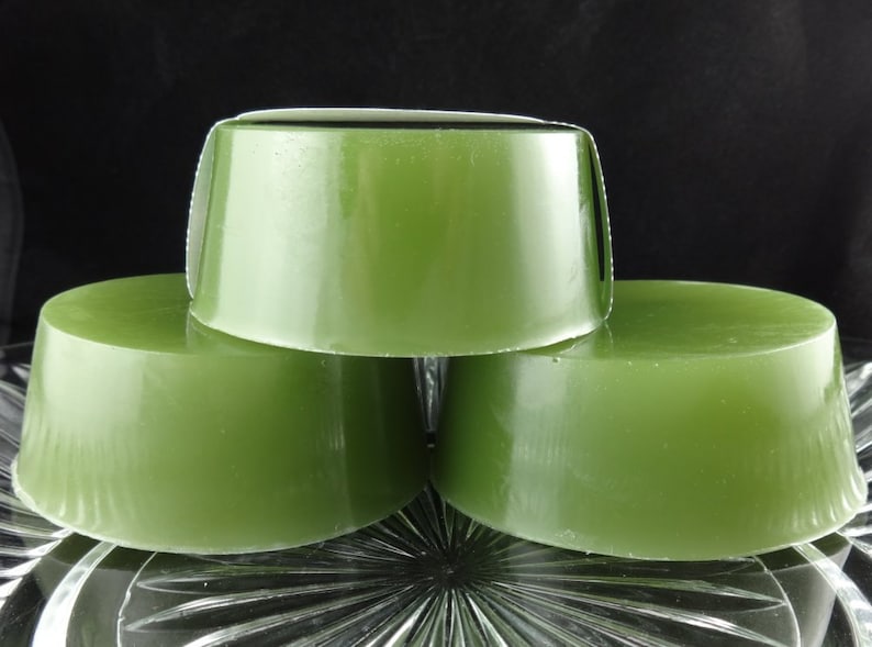 May include: Three round bars of green soap stacked on top of each other on a clear glass plate.