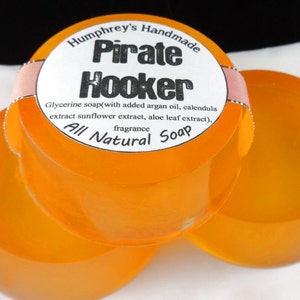 Pu&ograve; includere: Tre saponette arancioni fatte a mano con un'etichetta bianca che recita "Humphrey's Handmade Pirate Hooker Glycerine soap (with added argan oil, calendula extract sunflower extract, aloe leaf extract), fragrance All Natural Soap".