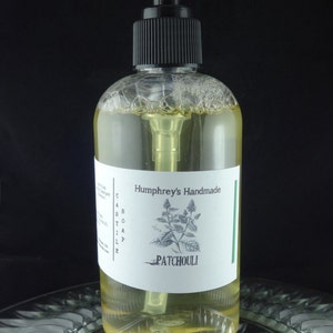 May include: A clear glass bottle with a black pump dispenser filled with a yellow liquid. The bottle has a white label with the text "Humphrey's Handmade" and "PATCHOULI" in black lettering. The label also features a black and white illustration of a plant.