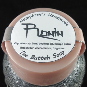 May include: A round, pink soap bar with a white label that reads "Humphrey's Handmade Plonin Glycerin soap base, coconut oil, mango butter shea butter, cocoa butter, fragrance The Buttah Soap".
