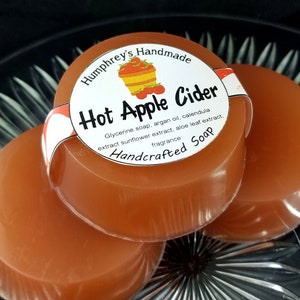 May include: Three round bars of handcrafted soap with a label that reads "Humphrey's Handmade Hot Apple Cider Glycerine soap, argan oil, calendula extract sunflower extract, aloe leaf extract, fragrance Handcrafted Soap".