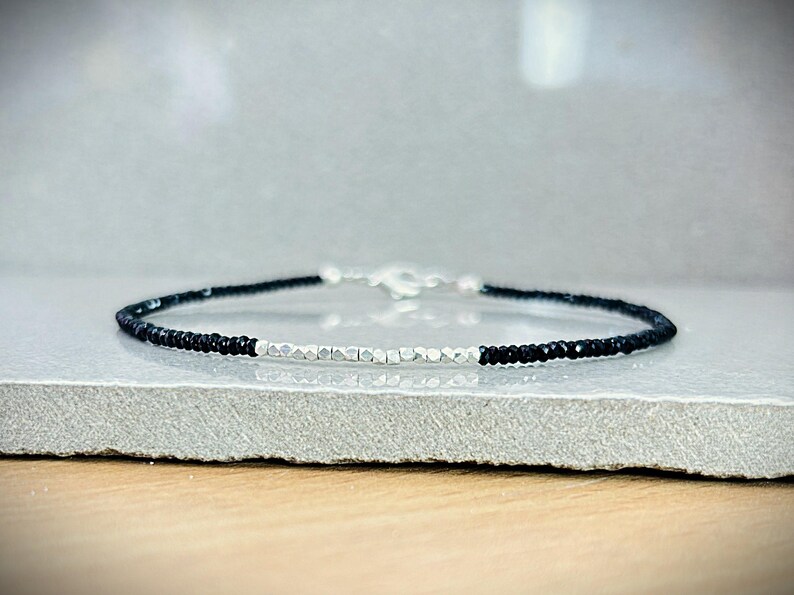 May include: A delicate bracelet featuring alternating sections of black and silver beads. The bracelet is secured with a silver clasp. The beads are small and evenly spaced, creating a minimalist and elegant design. The bracelet is displayed on a neutral surface.