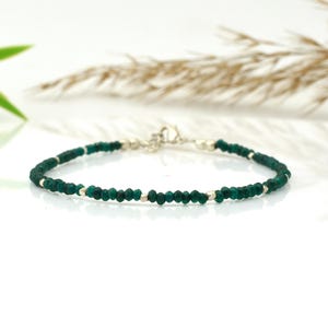 May include: A delicate bracelet featuring small, faceted emerald green beads strung together with silver-colored metal accents. The bracelet has a simple clasp closure and is displayed on a white surface. The jewelry is a classic accessory.