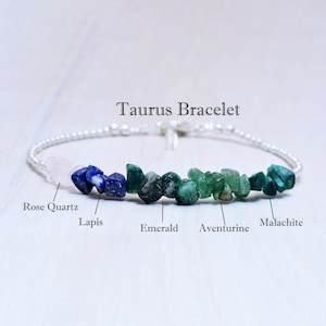 May include: A Taurus Bracelet featuring a string of small, round, silver beads. The bracelet includes Rose Quartz, Lapis, Emerald, Aventurine, and Malachite gemstones. The text "Taurus Bracelet" is displayed above the bracelet.