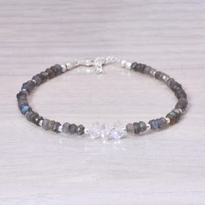 May include: A beaded bracelet featuring gray and iridescent labradorite stones interspersed with small silver beads. The bracelet also includes three clear, faceted crystal stones and a silver clasp.