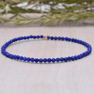 May include: A delicate bracelet featuring small, round, deep blue beads. The beads are strung together, forming a complete circle. The bracelet is set against a neutral background, highlighting the vibrant color of the beads.