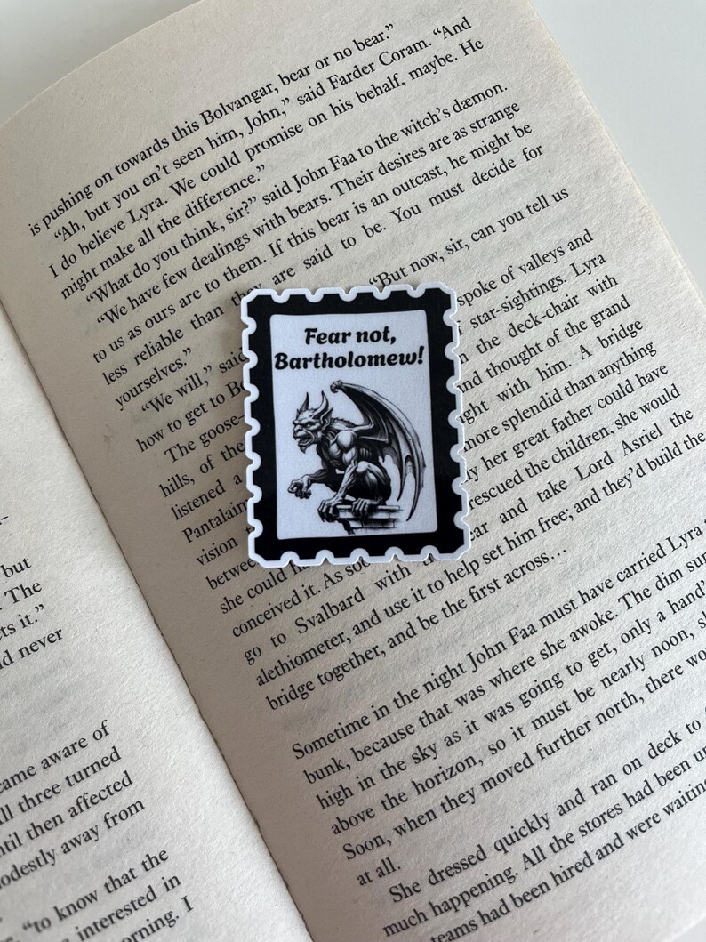 Puede incluir: Una pegatina rectangular con borde negro y bordes festoneados, que presenta una ilustraci&oacute;n en blanco y negro de una g&aacute;rgola posada en una repisa. El texto "Fear not, Bartholomew!" est&aacute; impreso en tinta negra sobre la ilustraci&oacute;n.