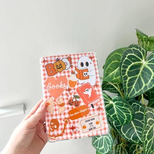 May include: Clear tablet case featuring a red and white gingham design and Halloween-themed stickers. Stickers include a ghost reading a book, a pumpkin, cherries, and the words "Boo!" and "Books."