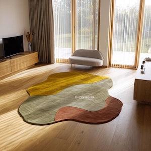 May include: An abstract rug with an irregular shape and a blend of colours. The rug incorporates mustard yellow, olive green, and rust-toned sections. The text "Ruggy world" is visible on the rug.