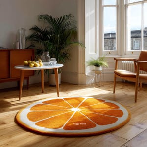 May include: A round orange slice rug with a white border sits on a hardwood floor. The rug's design features orange segments radiating from the center. The room includes a white table, wooden chair, and a large plant.