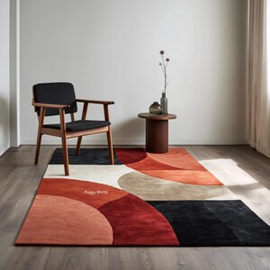Könnte beinhalten: Moderner rechteckiger Teppich mit geometrischem Design in Rot, Schwarz, Beige und Weiß. Der Teppich zeigt überlappende, gebogene Formen. Ein Holzstuhl mit schwarzem Sitz und ein kleiner Beistelltisch befinden sich neben dem Teppich.