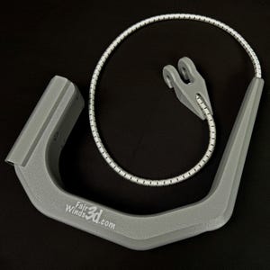 Pode incluir: Um componente cinza em forma de U impresso em 3D com o texto FairWinds3d.com impresso na lateral. Inclui um cord&atilde;o el&aacute;stico flex&iacute;vel com padr&atilde;o branco e cinza preso a uma pequena pe&ccedil;a de conex&atilde;o cinza em forma de garfo na extremidade.