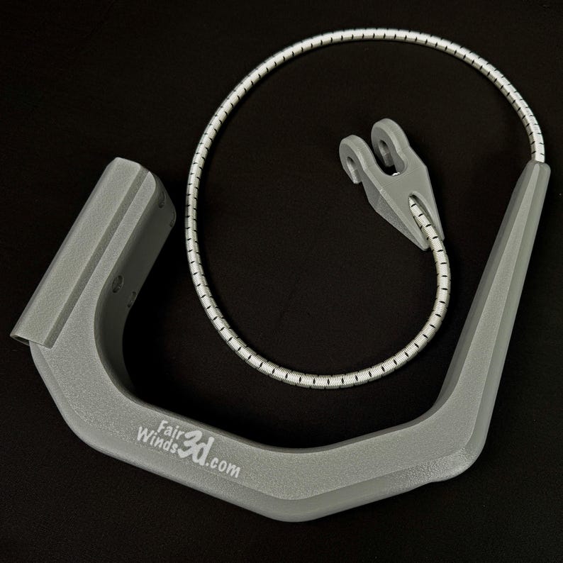 Pode incluir: Um componente cinza em forma de U impresso em 3D com o texto FairWinds3d.com impresso na lateral. Inclui um cord&atilde;o el&aacute;stico flex&iacute;vel com padr&atilde;o branco e cinza preso a uma pequena pe&ccedil;a de conex&atilde;o cinza em forma de garfo na extremidade.