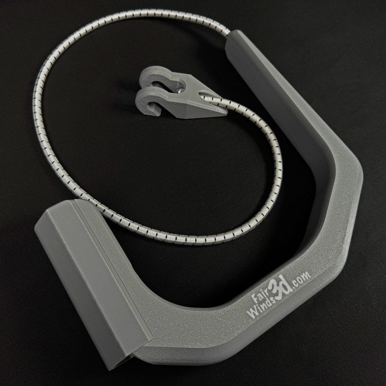 Pode incluir: Uma al&ccedil;a cinza em forma de U com acabamento texturizado e o texto FairWinds3D.com impresso na lateral. Inclui um cord&atilde;o el&aacute;stico flex&iacute;vel prateado e branco preso &agrave; al&ccedil;a, com um pequeno componente de gancho de pl&aacute;stico cinza em forma de V.