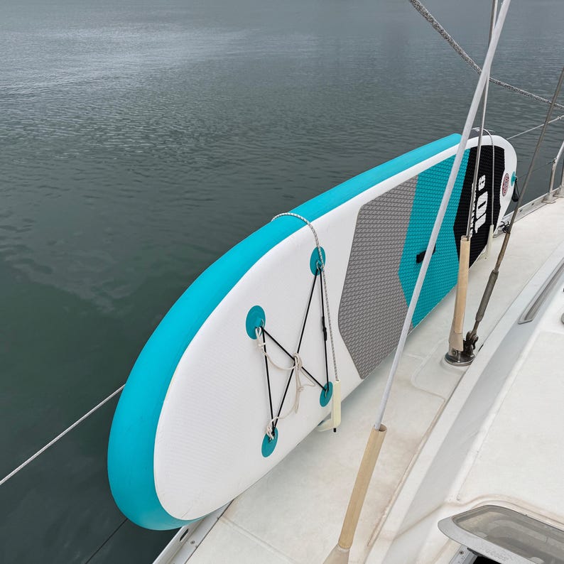 Pode incluir: Uma prancha de stand-up paddle infl&aacute;vel com um esquema de cores branco, turquesa e cinza e um deck pad texturizado. A prancha inclui um sistema de cordas el&aacute;sticas pretas para armazenamento e exibe o texto 10'6 na superf&iacute;cie.