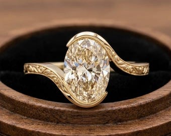 May include: A gold engagement ring with an oval-cut diamond. The ring features a swirling design with intricate filigree detailing on the band. The diamond is a light champagne color, set in a delicate, curved setting.