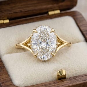 Peut inclure: Bague de fiançailles en or avec un diamant de taille ovale. La bague est ornée d'un halo de petits diamants et d'une monture fendue. Présentée dans un écrin en bois avec intérieur crème.