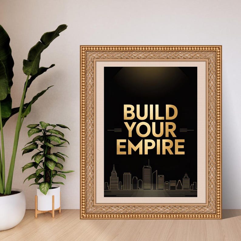May include: A framed wall art piece featuring a black background with the gold text BUILD YOUR EMPIRE centered above a gold line-art city skyline. The artwork is enclosed in an ornate, textured gold frame with a light-colored matting border.