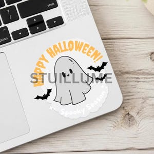 May include: A circular sticker featuring a light gray ghost with a smiling face, surrounded by black bats and orange text that reads Happy Halloween! and white text that reads Spooky Season, all set against a white background on a laptop.