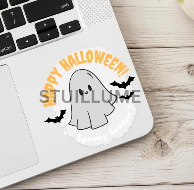 May include: A circular sticker featuring a light gray ghost with a smiling face, surrounded by black bats and orange text that reads Happy Halloween! and white text that reads Spooky Season, all set against a white background on a laptop.
